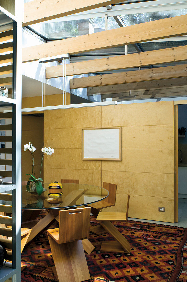 Glastisch mit Designerstühlen vor Schiebeelement aus Holz in elegantem Architektenhaus