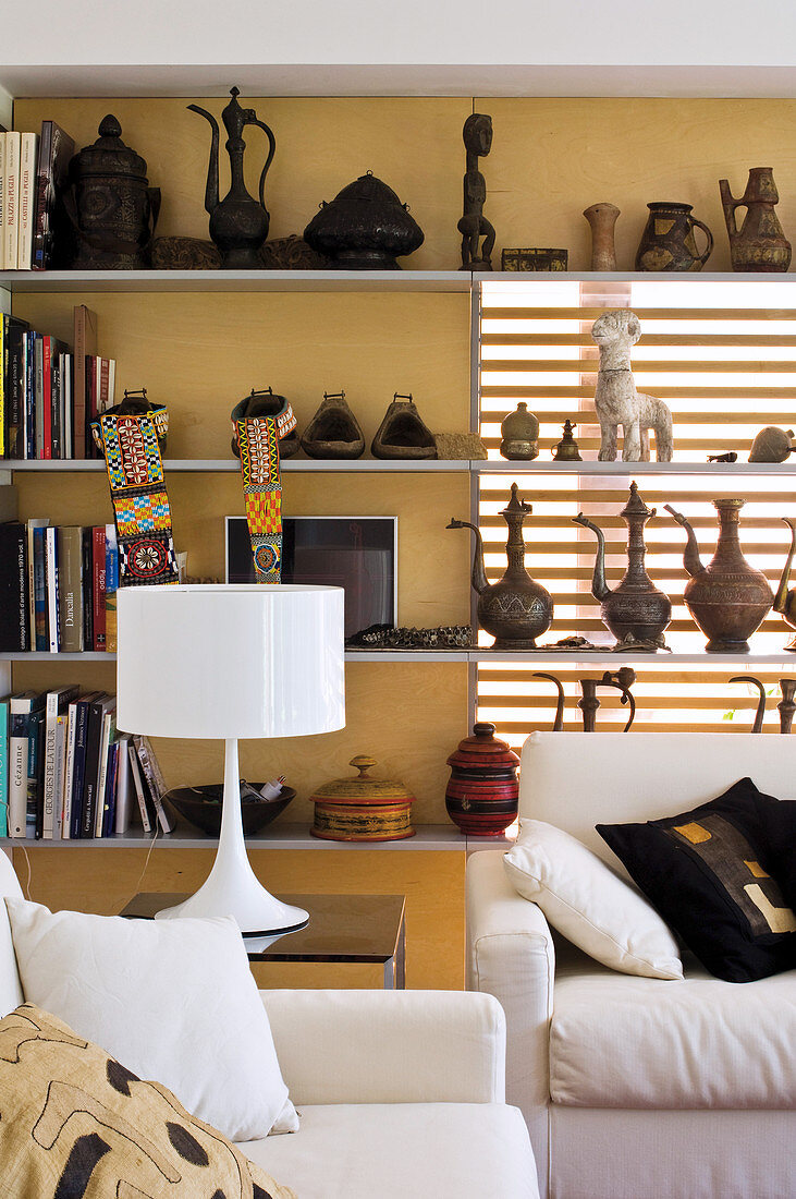 Various collections on wall-mounted shelves, white table lamp on side table and sofa set