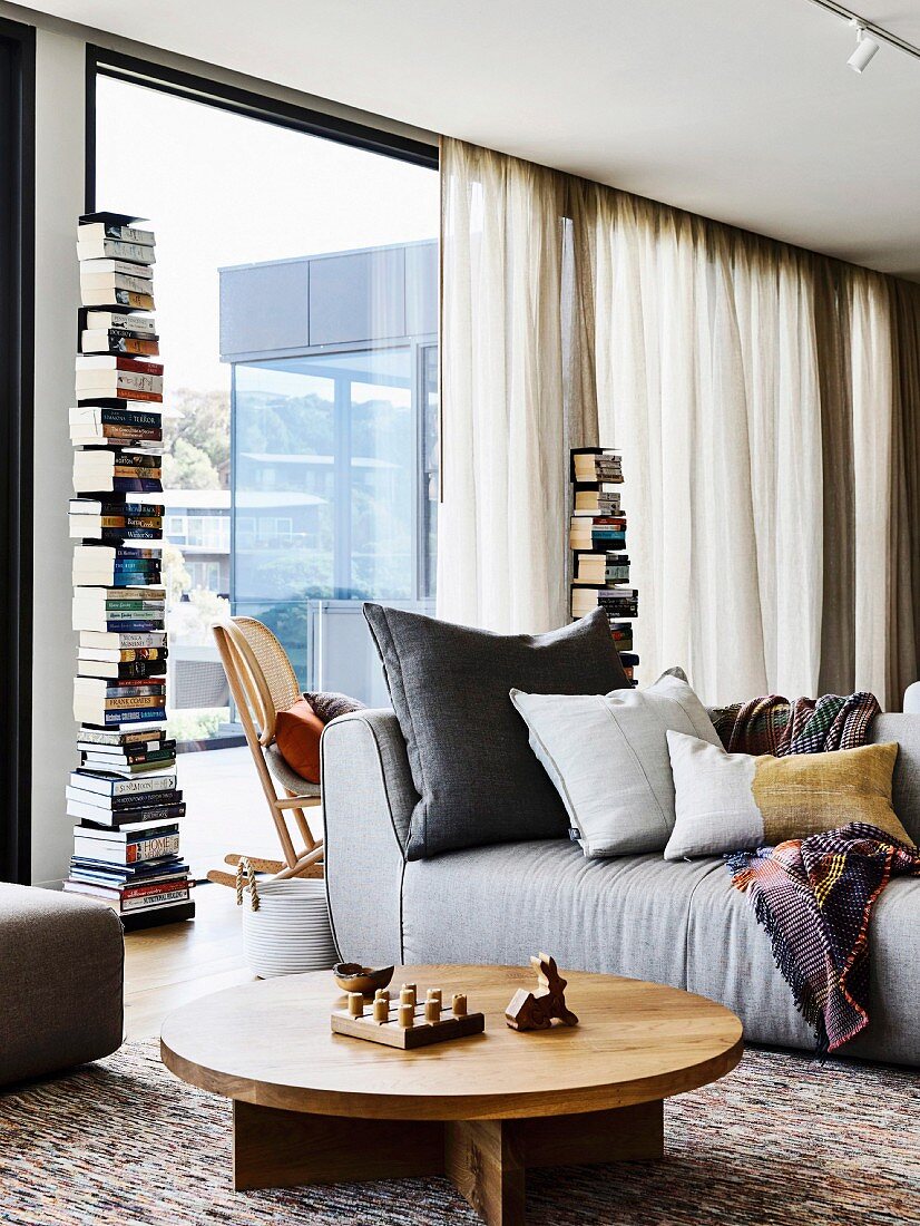Living room with upholstered sofa, round wooden table and bookcase in front of a window