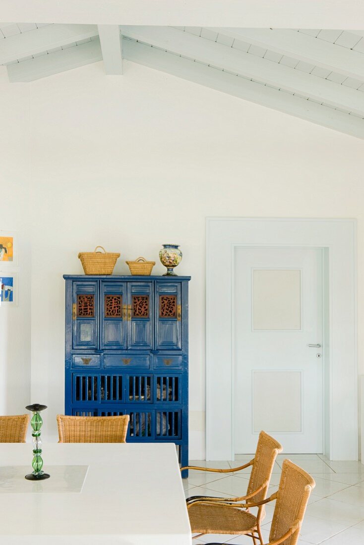 Weisses Esszimmer mit traditionellem, blauem Schrank und Korbstühlen