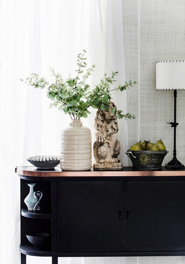 Black sideboard with decorative objects in front of a window
