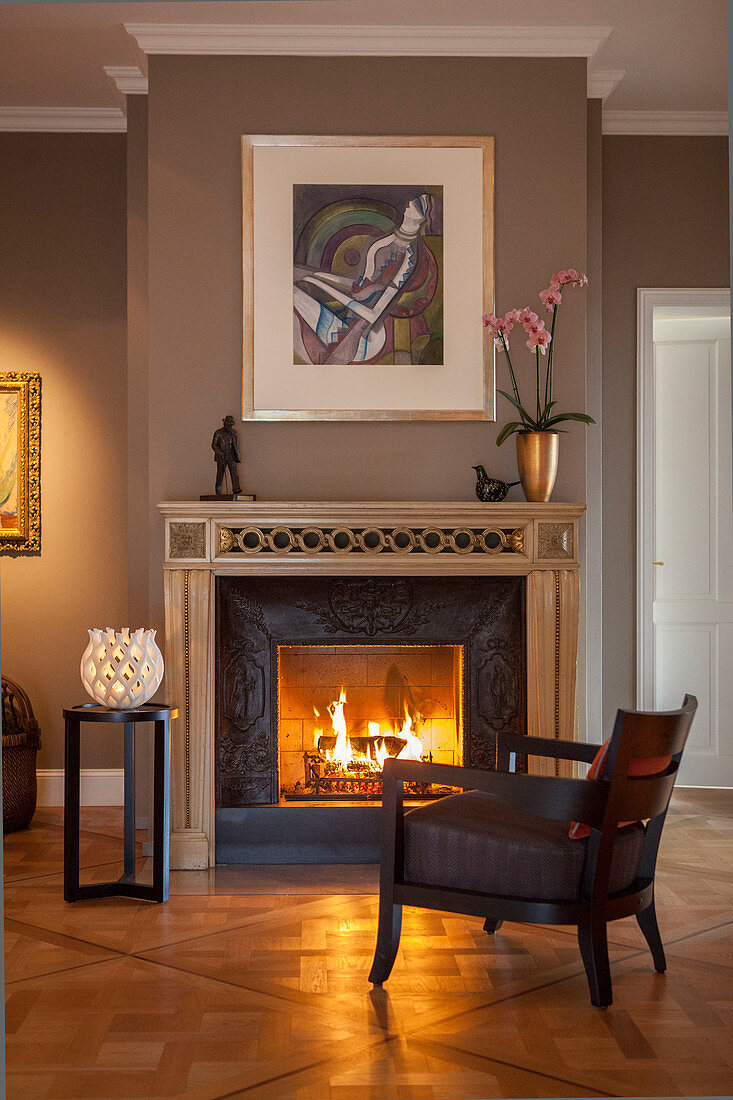 Upholstered armchair in front of roaring fire in open fireplace