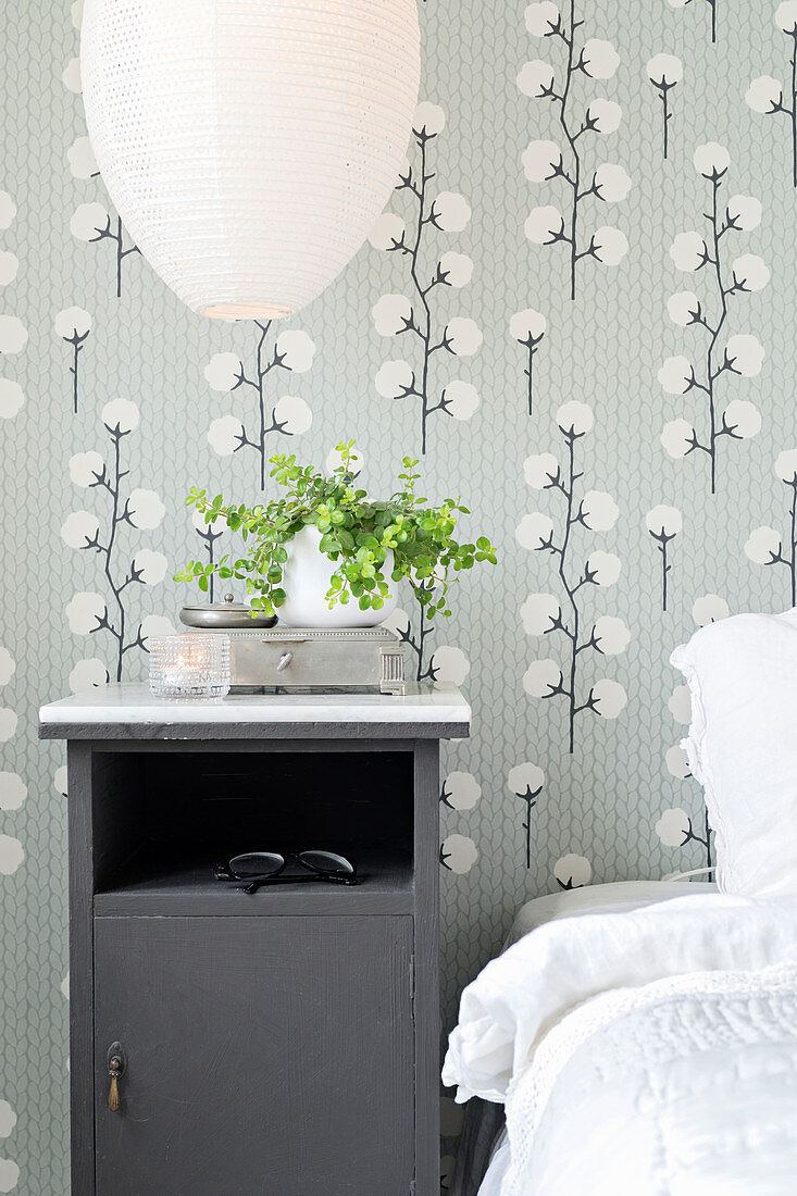 Grey bedside cabinet against wallpaper with pattern of cotton plants