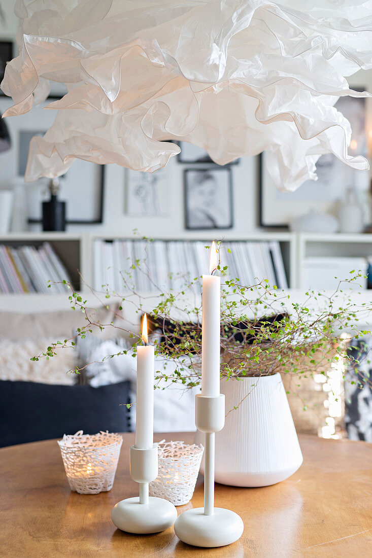 White candles and tealight holders on coffee table below paper lamp