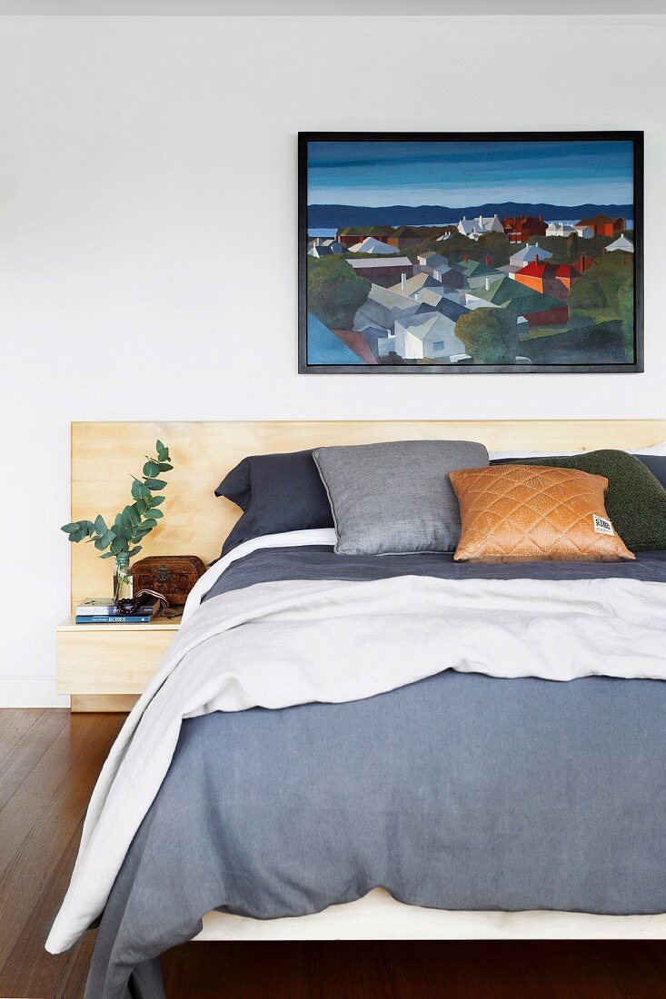 Double bed with various pillows under a black framed painting