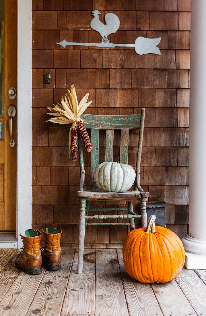 Pumpkins, dried maize cobs and boots on porch in autumn