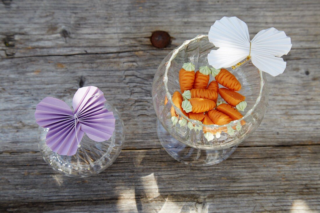 Schmetterlinge aus gefaltetem Papier an Gläsern mit Zuckerkarotten