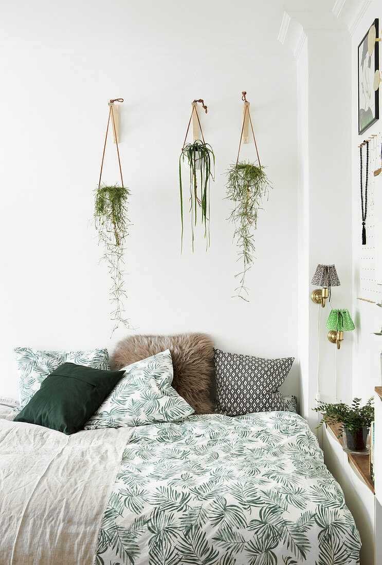 Blumenampeln mit Hängepflanzen über dem Bett mit Blattmotiv