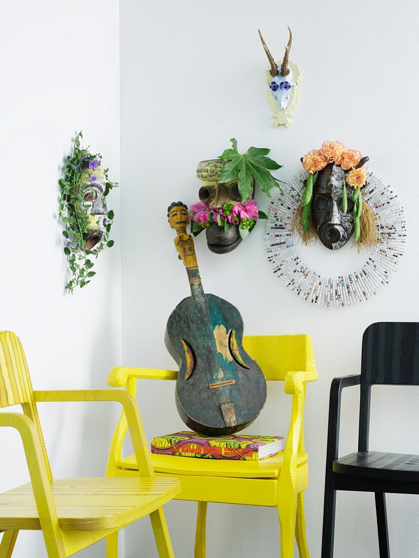 Verschiedene Ethno-Tiermasken mit Blumendekoration über gelben Armlehnstühlen mit Ethno-Gitarre