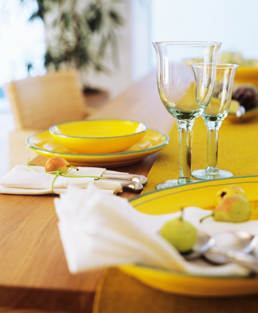 Gedeck mit gelbem Geschirr, Gläsern und Besteck in Stoffserviette