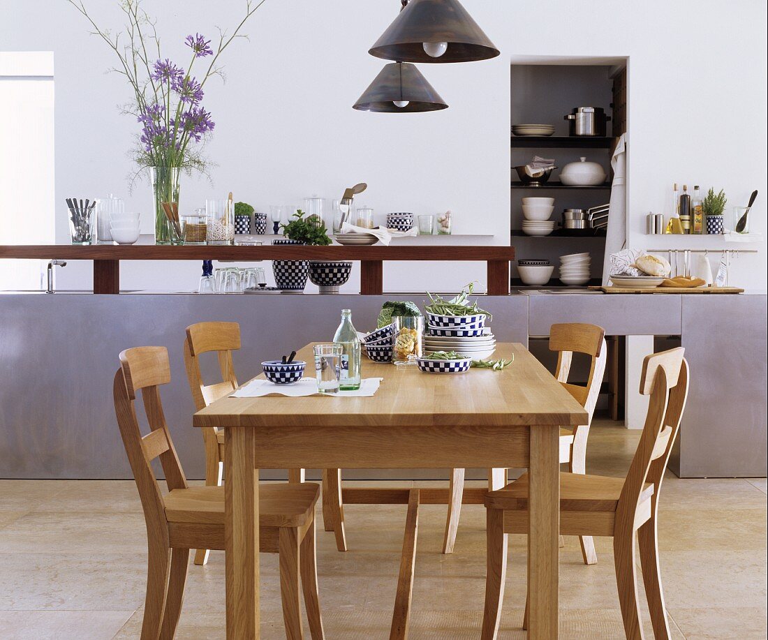 Eichentisch mit Stühlen vor eleganter Küchentheke und Wandnische mit Geschirrstapeln