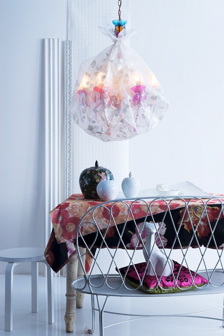 Embroidered silk chandelier above dining table with lidded jars on floral tablecloth