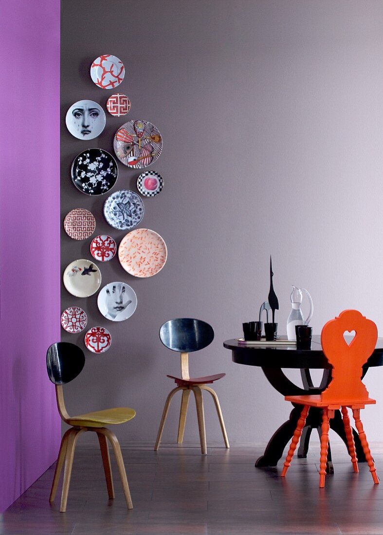 Vertical arrangement of designer wall plates on grey wall, designer chair and black round table