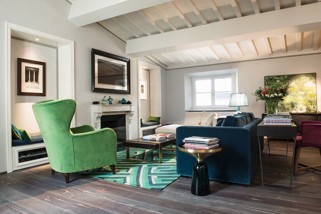 Grüner Ohrensessel und blaues Polstersofa mit Konsolentisch an der Rückseite in Wohnraum mit weisser Holzbalkendecke