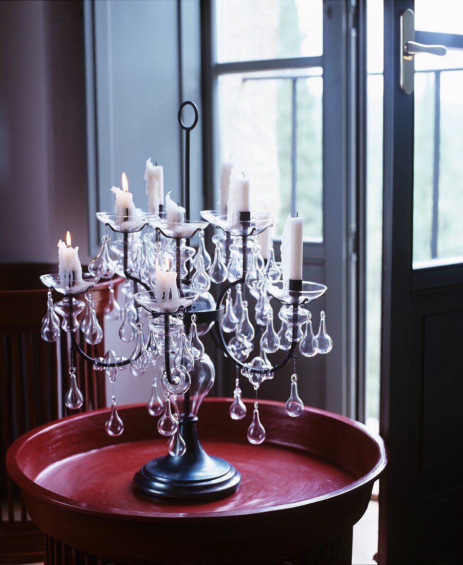 Mehrarmige Kerzenständer mit Kerzenschein auf rotem Tablett vor offener Fenstertür