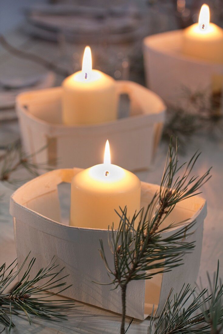 Brennende Kerzen in Spankörbchen und Kiefernzweige als Tischdekoration