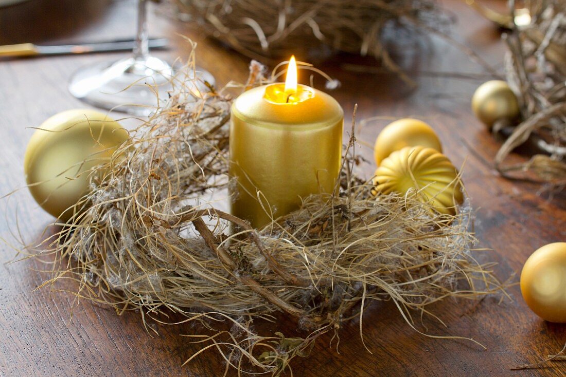 Goldfarbene Kerze in Kränzchen auf Holztisch mit Weihnachtskugeln dekoriert