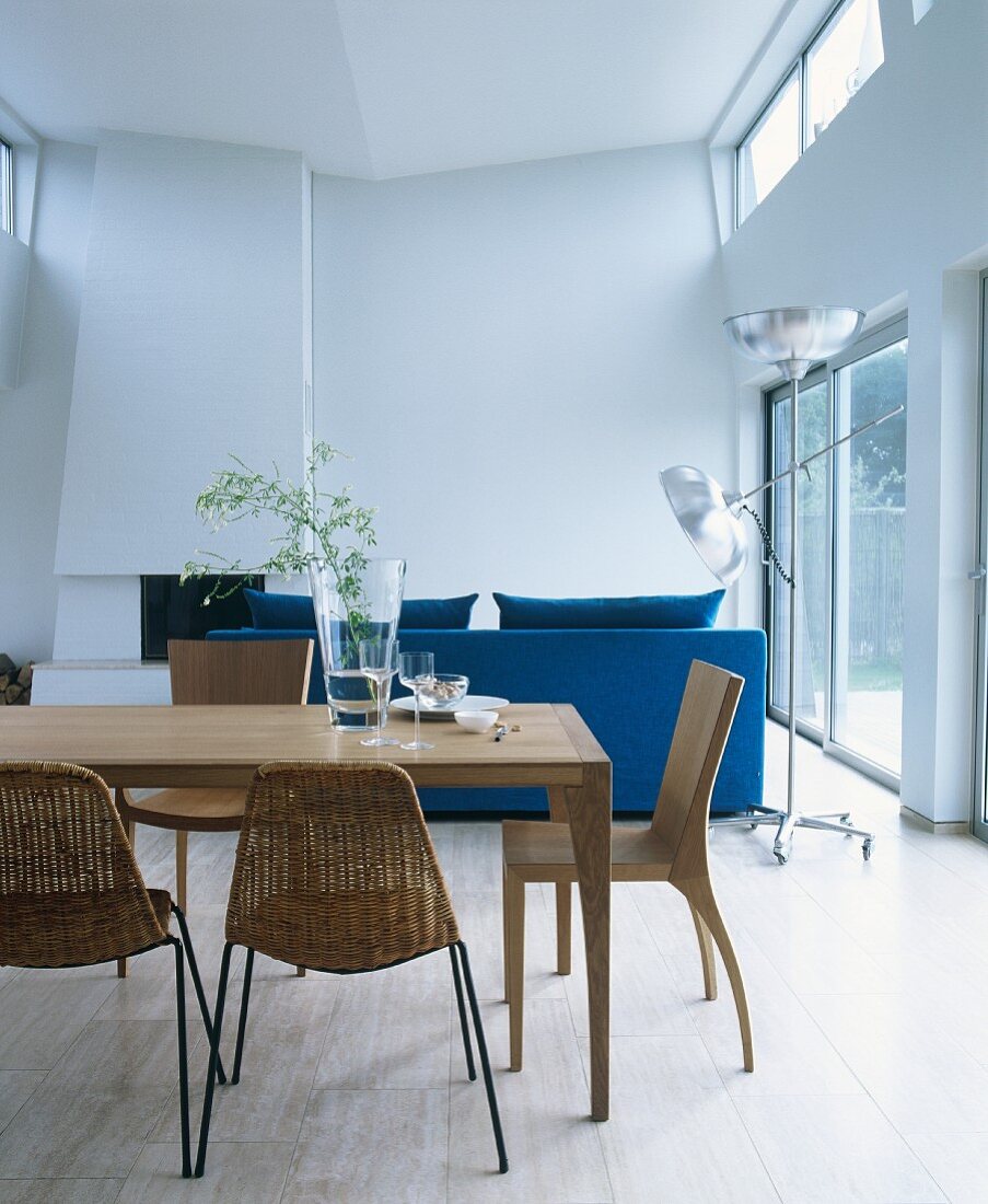 Holztisch mit verschiedenen Stühlen und blauer Polstersofa in offenem Wohnbereich mit Oberlichtband und Kamin