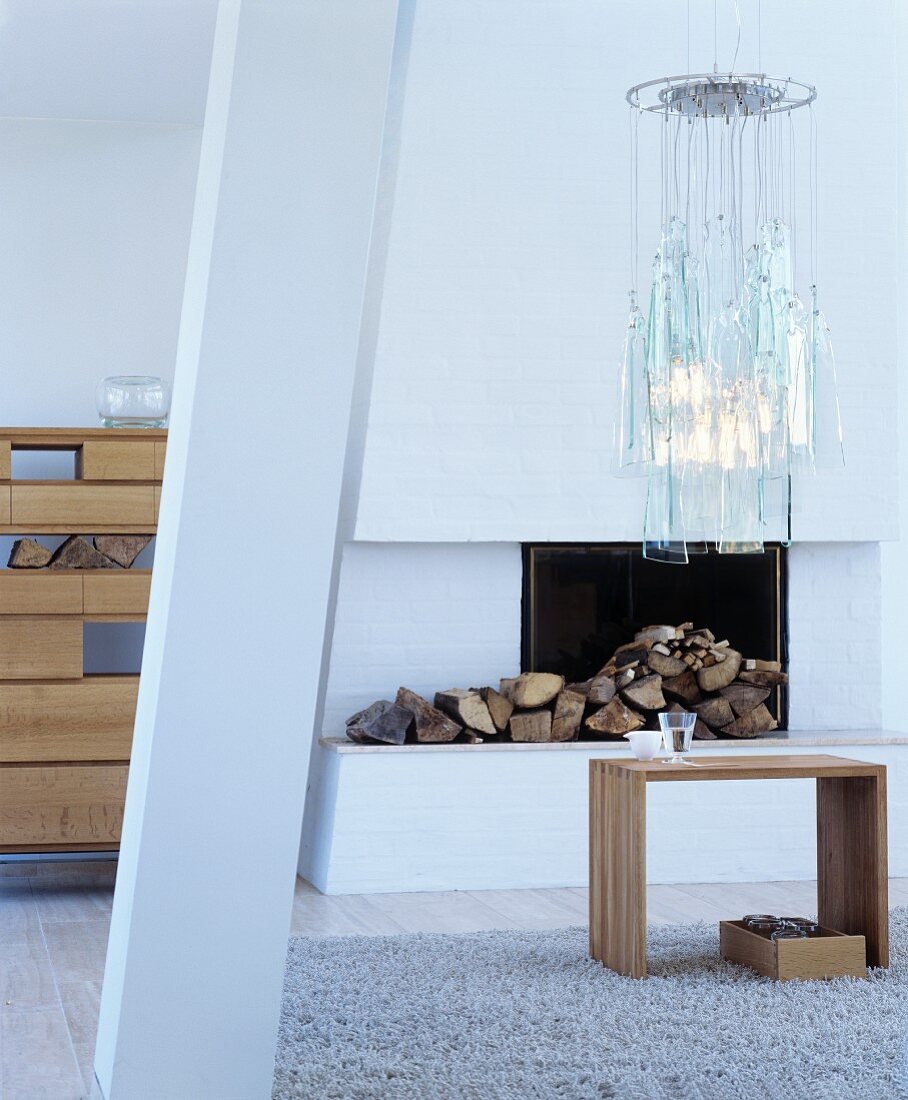 Wooden stool used as side table in front of white open fireplace below pendant lamp