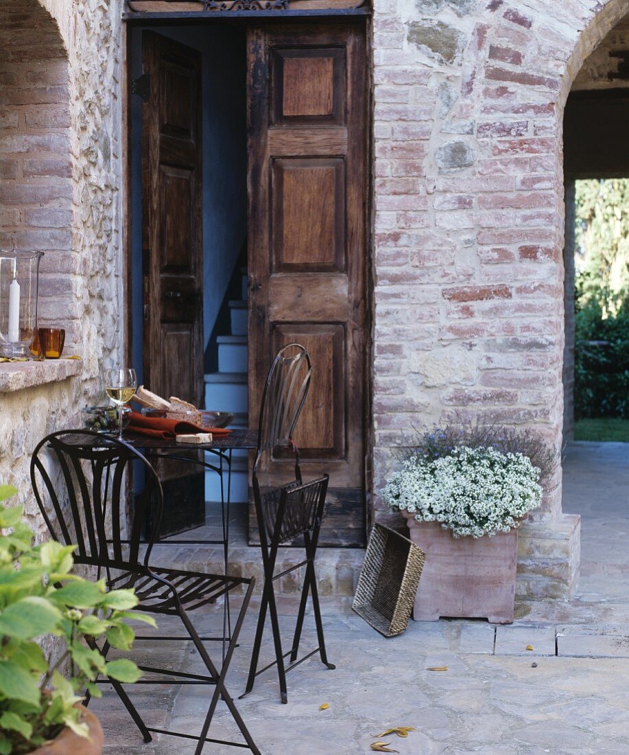 Filigrane, klappbare Metall-Outdoormöbel vor traditionellem, mediterranem Hauseingang