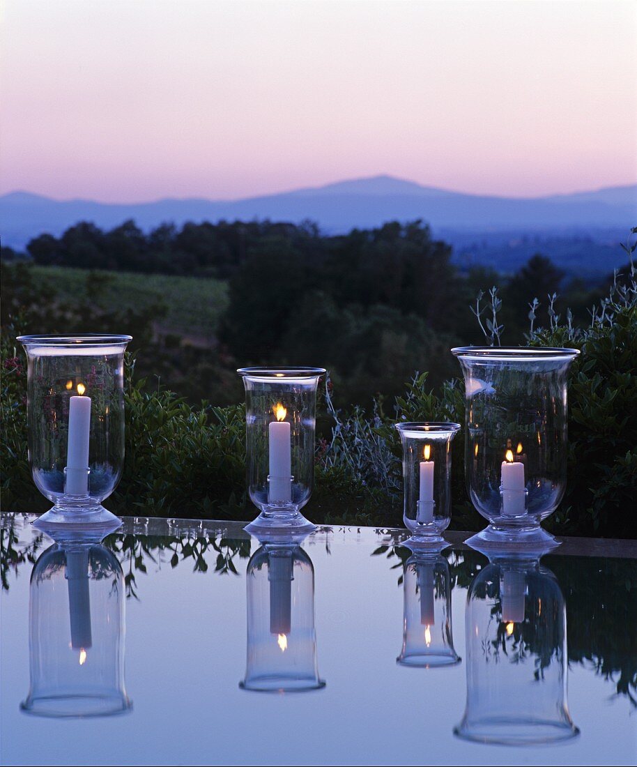 Lit candle lanterns reflected in surface of water in front of Mediterranean landscape