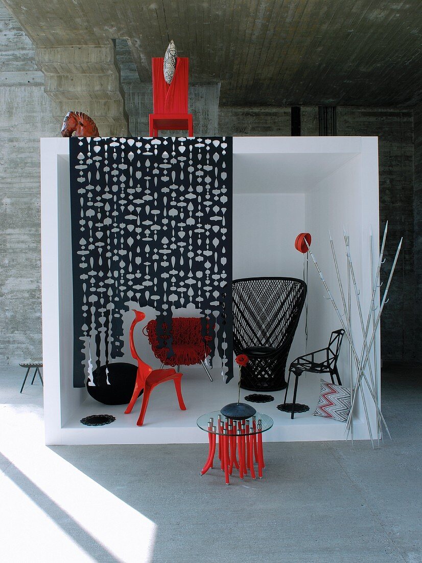 Schwarze und rote Designermöbel in weißem Kubus vor Betonwand