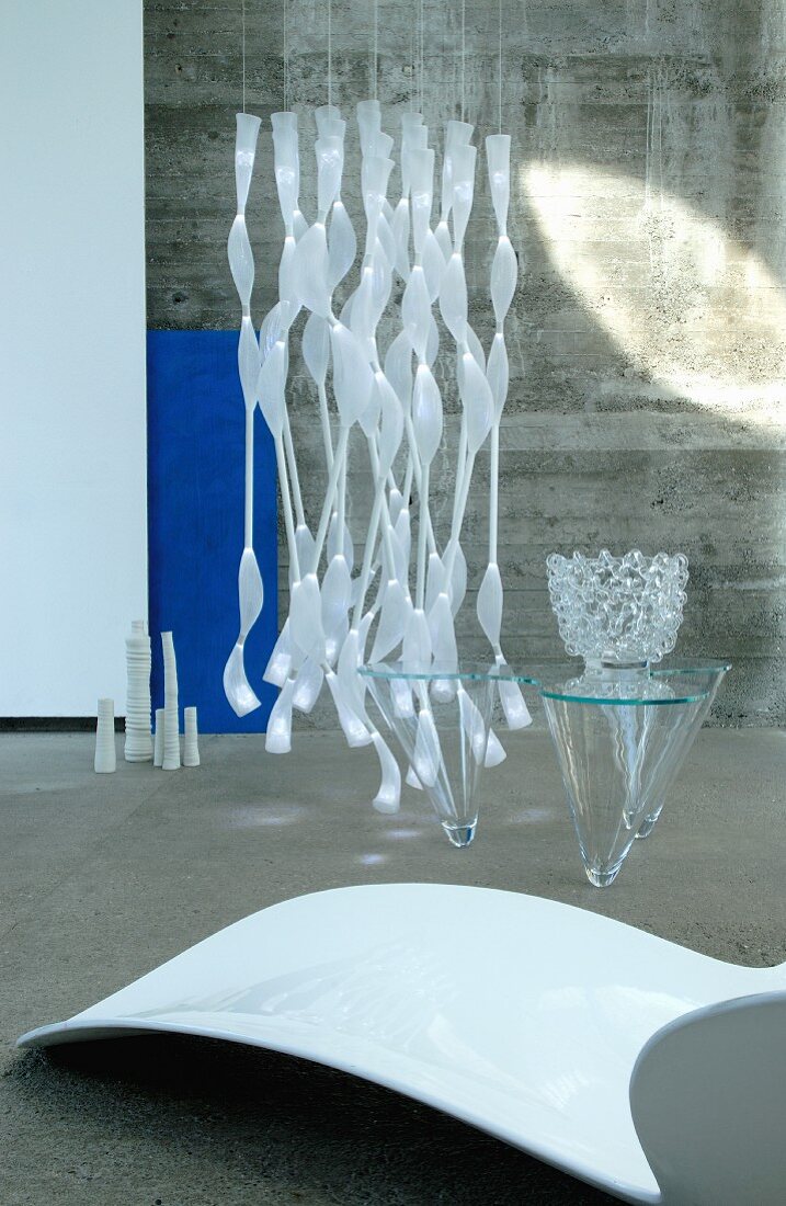 weiße Liege und Glastisch vor Designer-Pendelleuchte und Betonwand