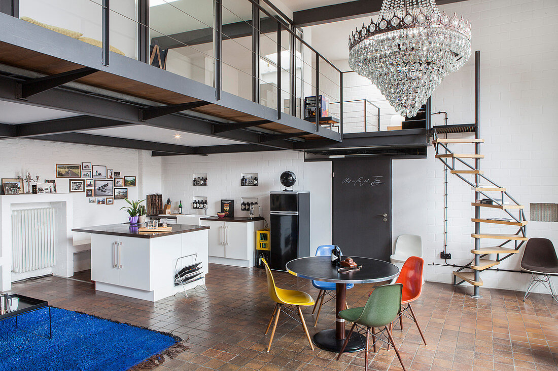 Open-plan kitchen and round dining table with designer chairs in industrial loft apartment