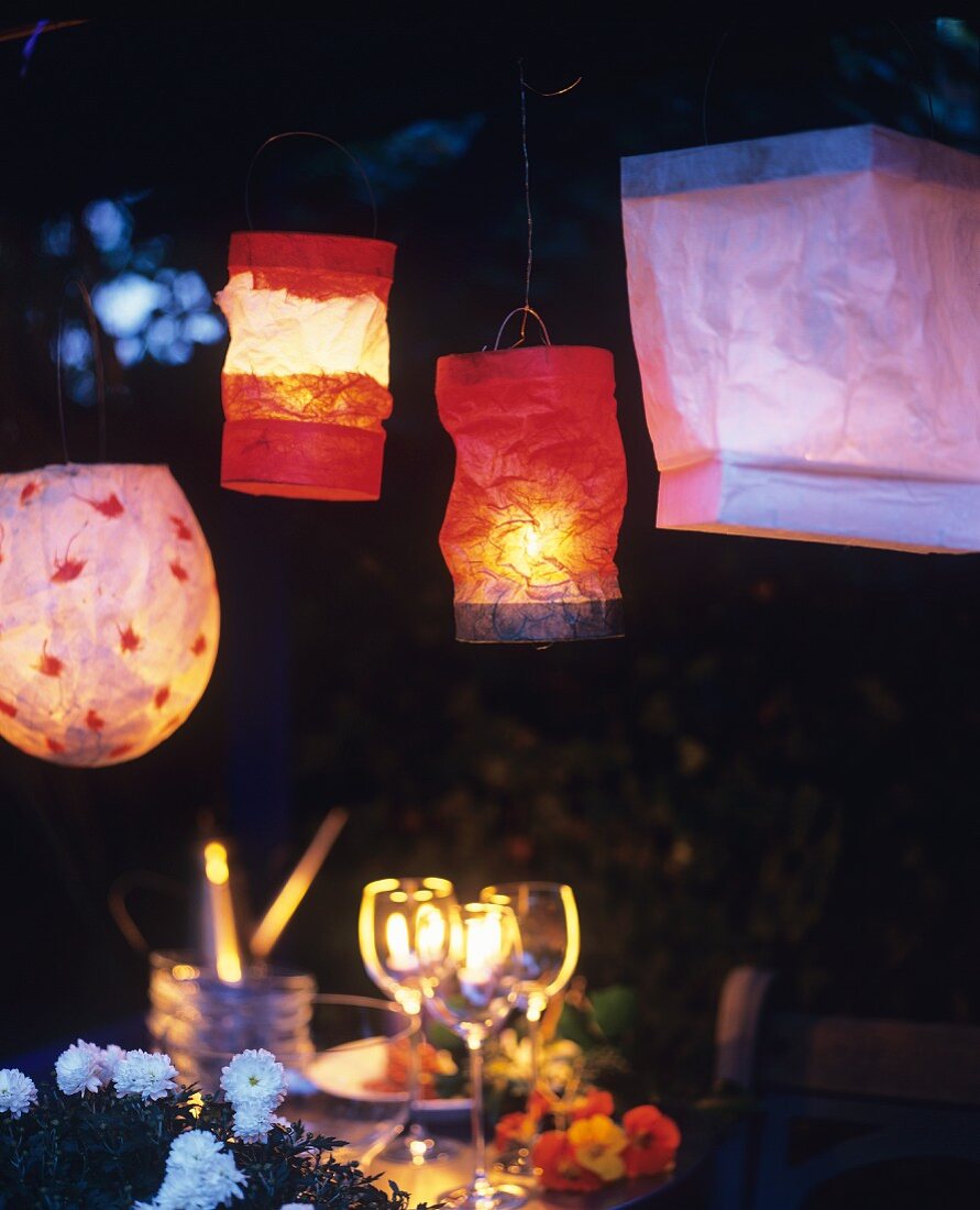 Various paper lanterns above set table in garden at twilight