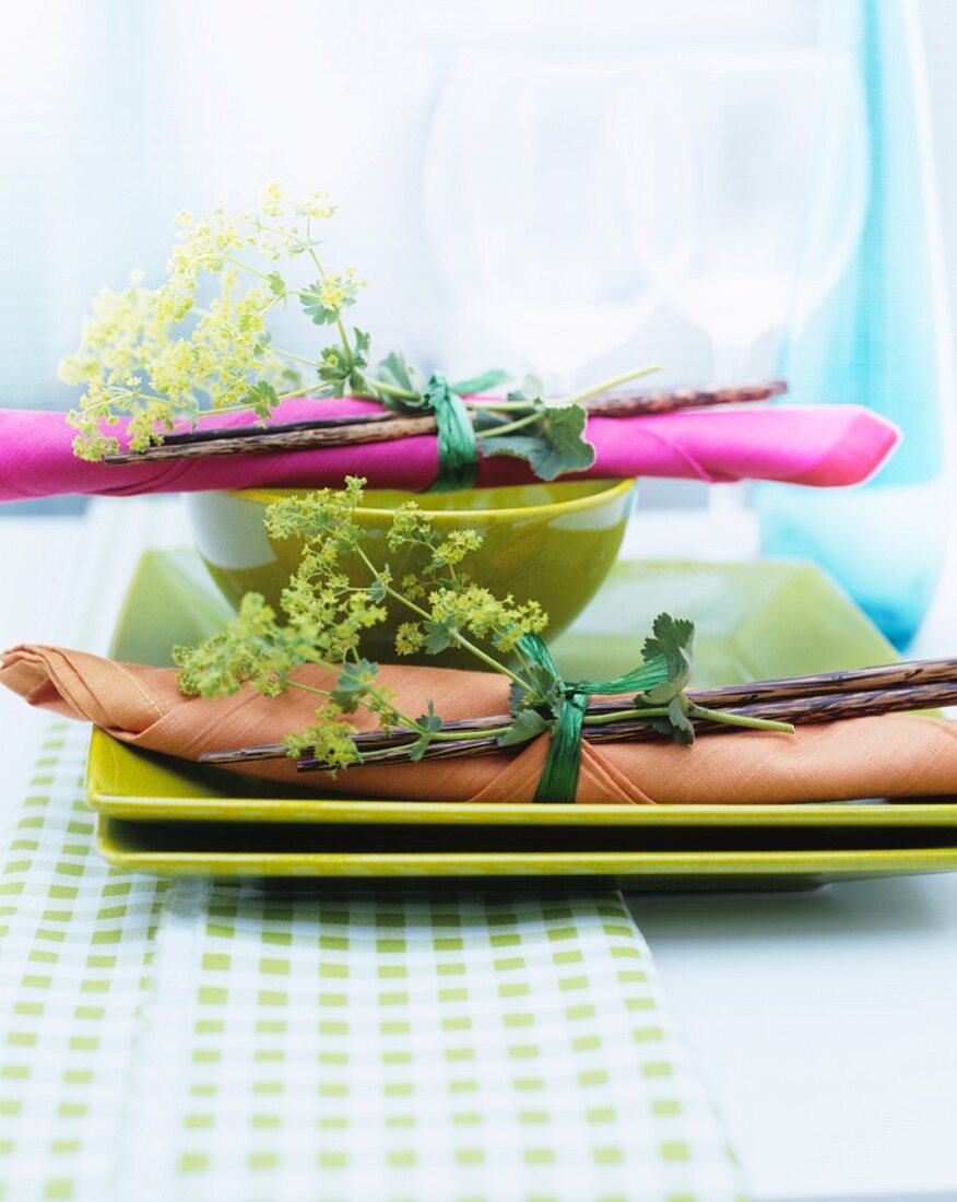Bündel aus Frauenmantel, Serviette und Essstäbchen auf grünen Tellern