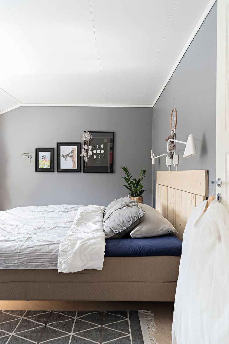 Bett mit Betthaupt aus Holz im Schlafzimmer mit grauen Wänden