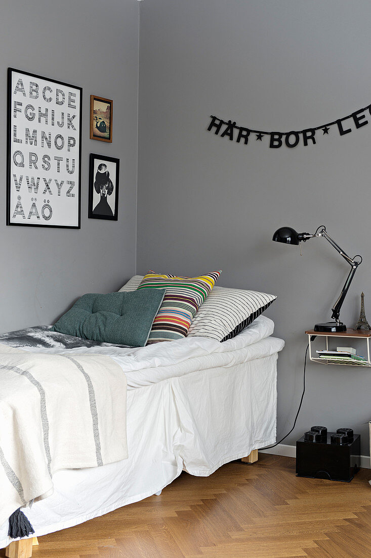 Buchstabengirlande über dem Bett mit Volant vor grauer Wand