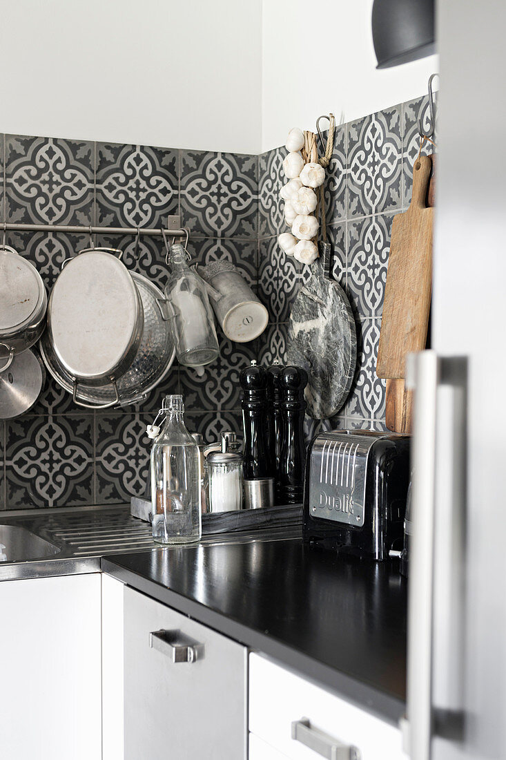 Kitchen utensils hung from rod on ornate, black-and-white, tiled splashback