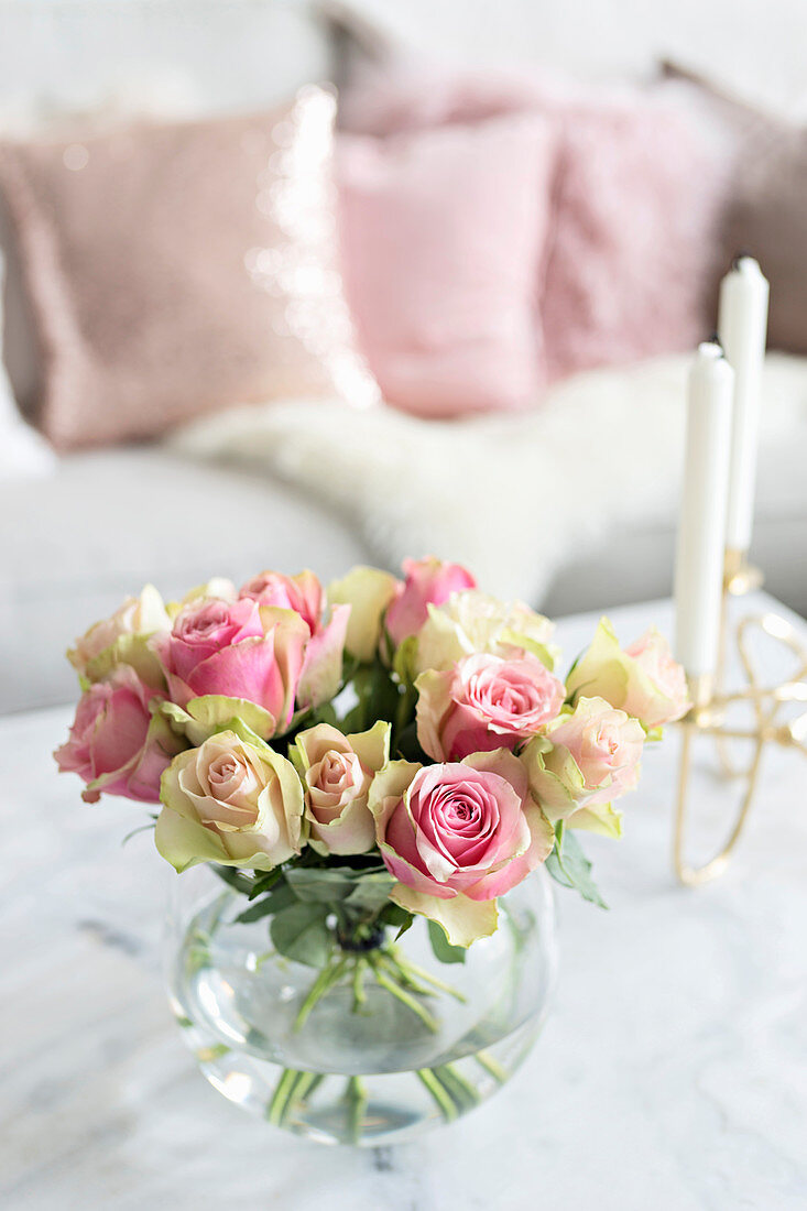 Spherical vase of roses and candelabra on coffee table in front of sofa with scatter cushions