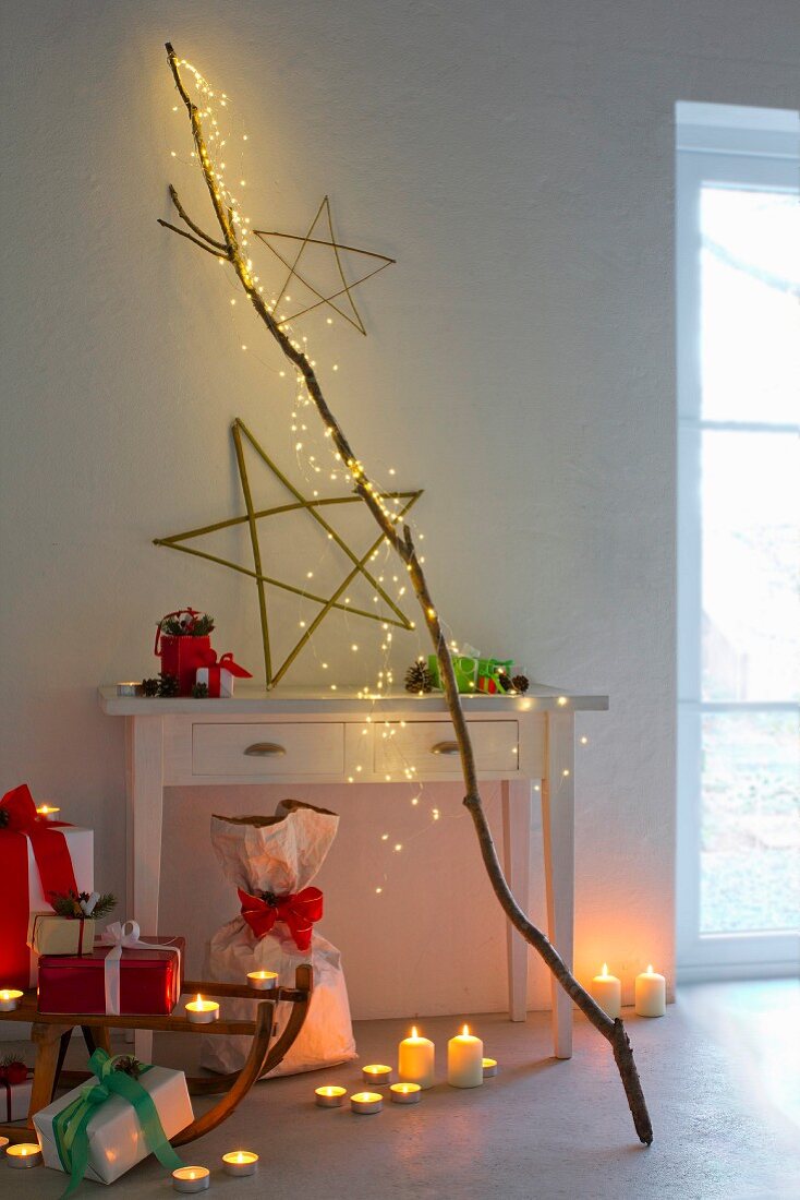 Stimmungsvolle Weihnachtsdekoration: LED-Lichterkaskade am Ast, Sterne aus Weidenästen, Teelichter, Kerzen und Weihnachtsgeschenke