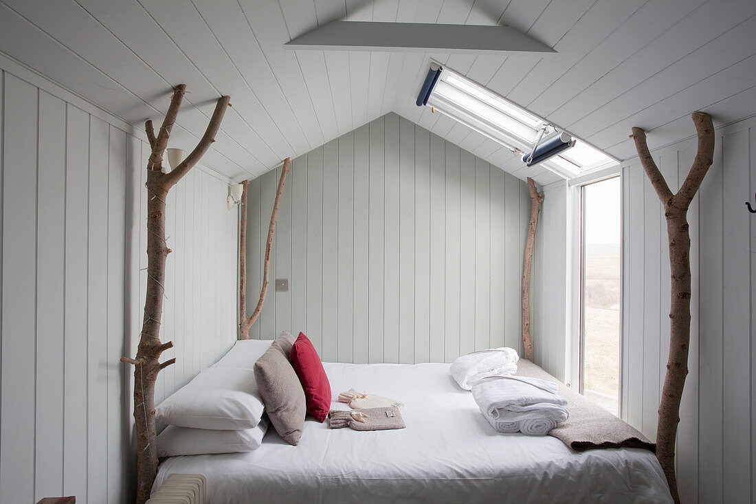 Bed with branches used as corner posts in tiny house with wood-clad walls