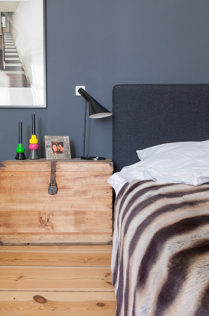 Holzkiste als Nachttisch neben dem Bett vor grauer Wand