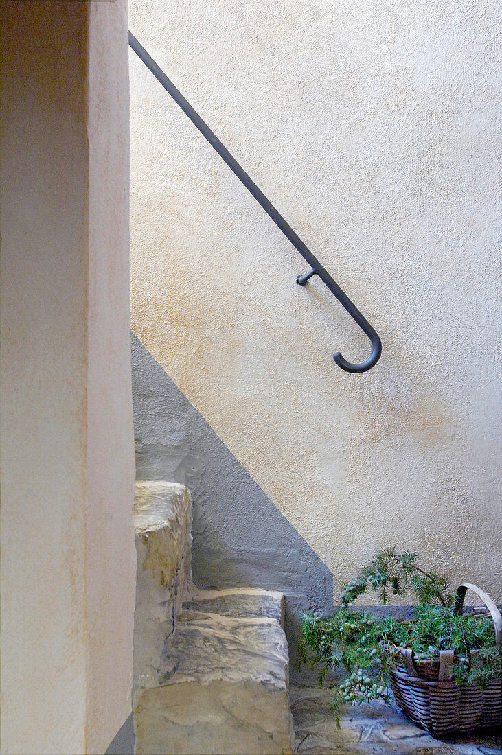 Korb mit Zweigen vor der Treppe an Wand mit gemaltem Sockel
