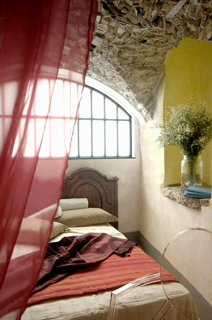 Bett vor einem Bogenfenster unter dem Gewölbe aus Naturstein