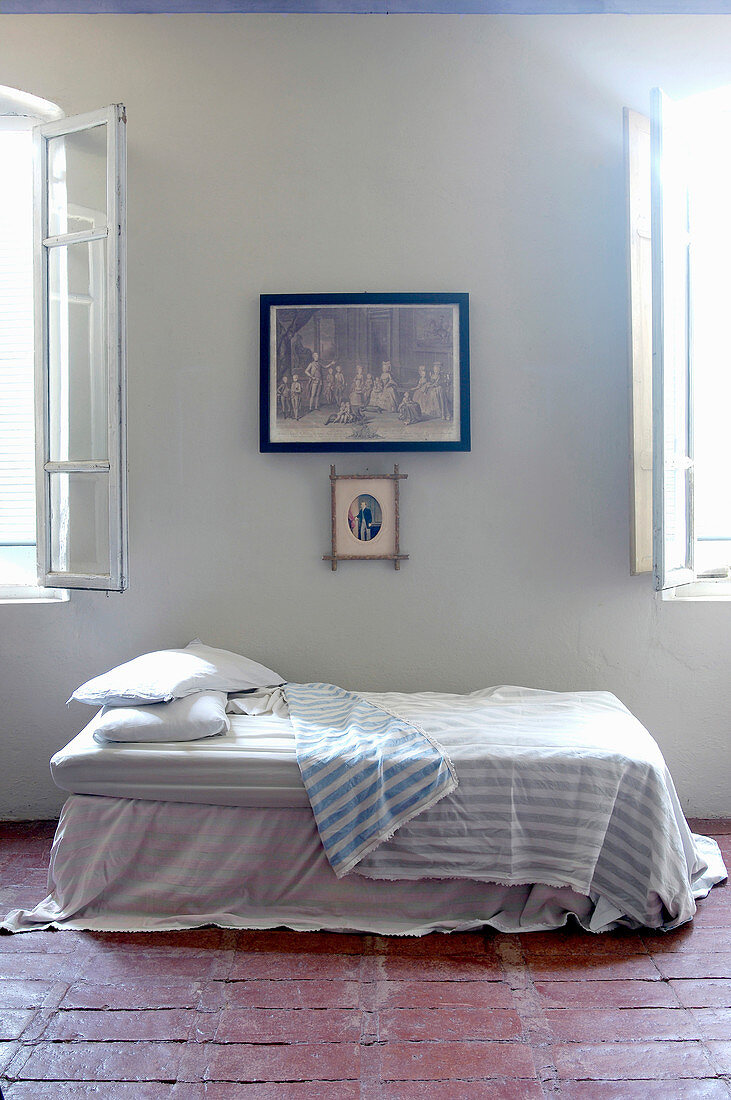 Bett mit Überwurf zwischen zwei Fenstern auf Terracottafliesenboden