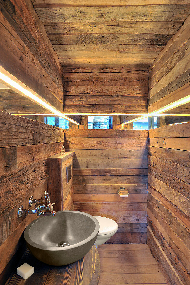 Narrow mirrored strip running along three rustic wooden walls in bathroom