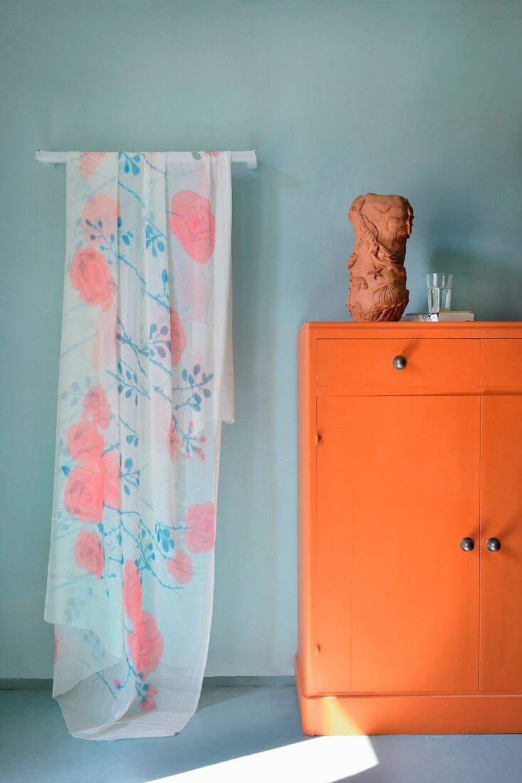 Zartes geblümtes Tuch hängt neben orangefarbenem Schränkchen