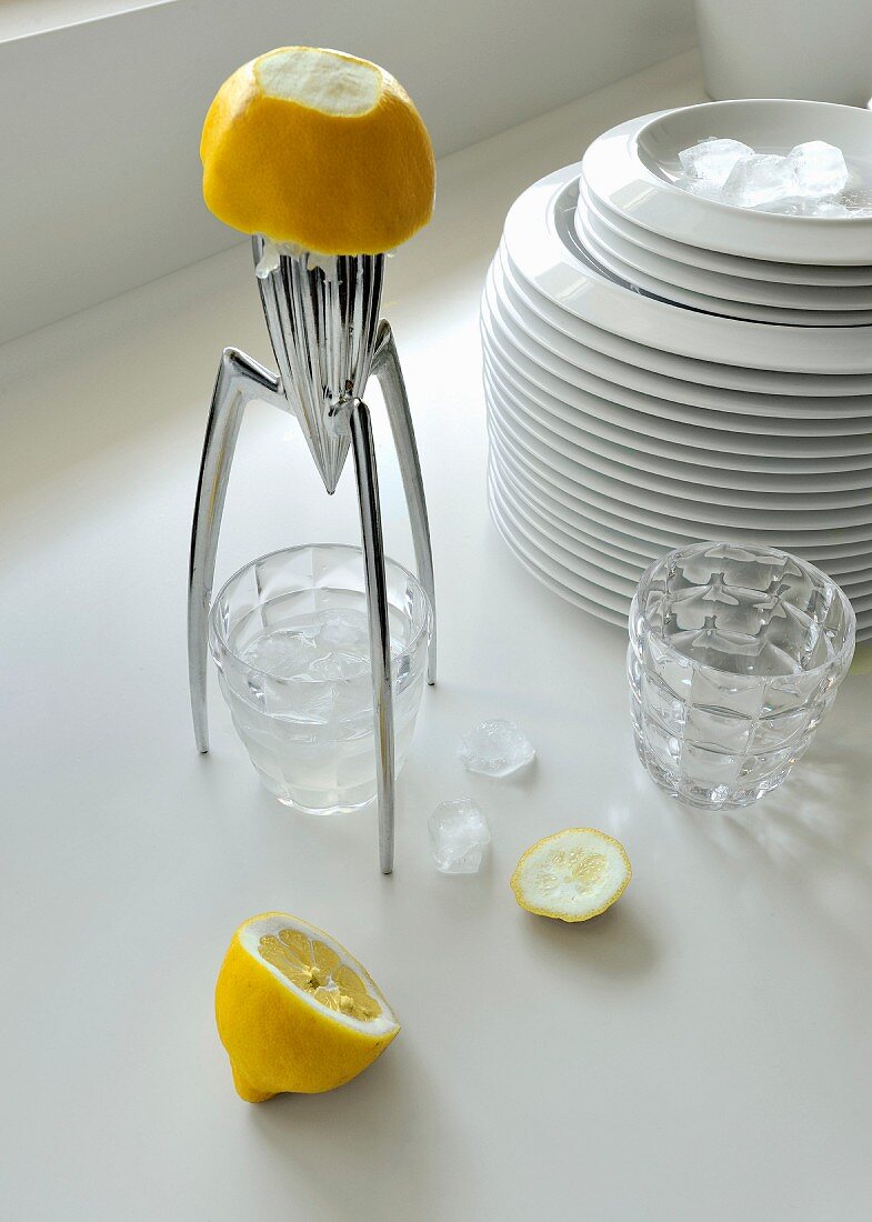 Futuristische Zitronenpresse, halbierte Zitrone und Wassergläser