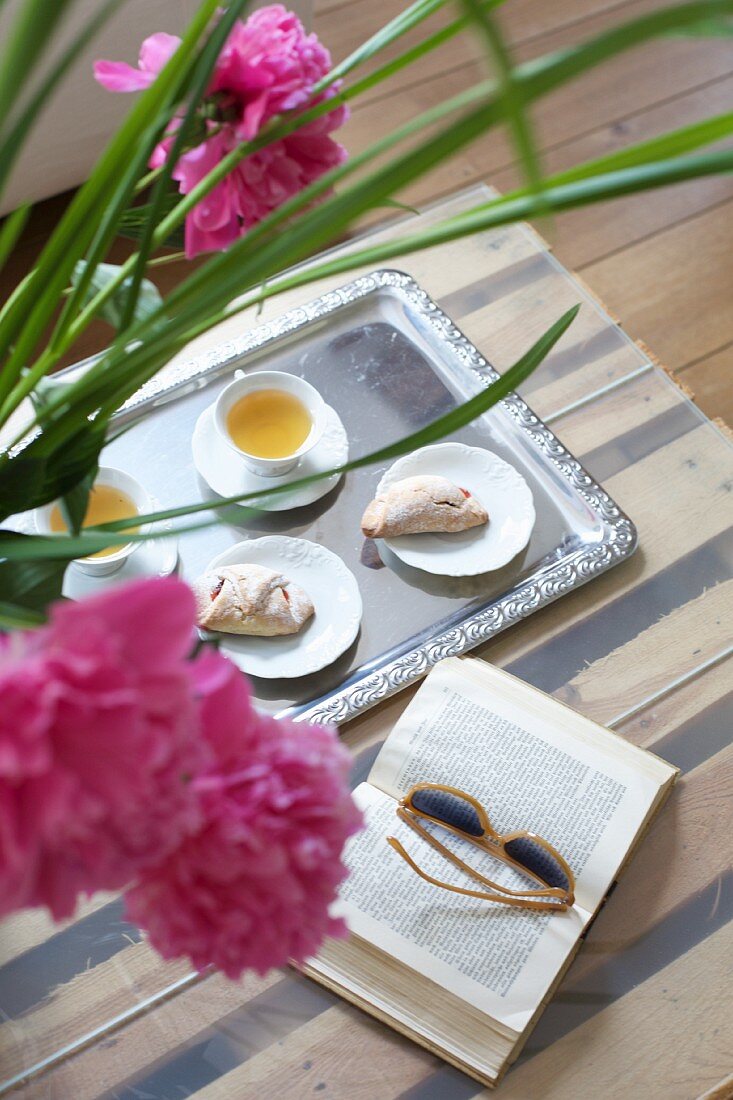 Pastries and tea on tray next to book and pink peonies