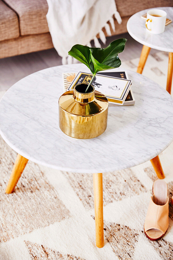 Goldfarbene Blumenvase mit einem Blatt auf Coffeetable mit Marmorplatte