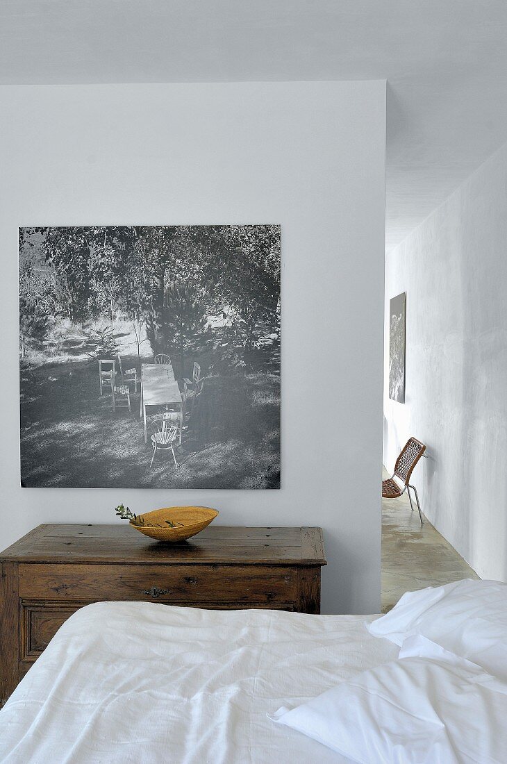 Reduzierter Schlafbereich mit antiker Holztruhe und schwarz-weisser Aufnahme an Wand