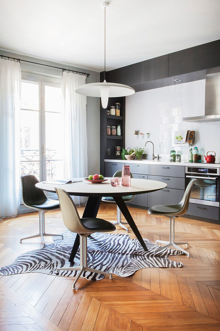 Round dining table and retro chairs on zebra-skin rug in grey fitted kitchen
