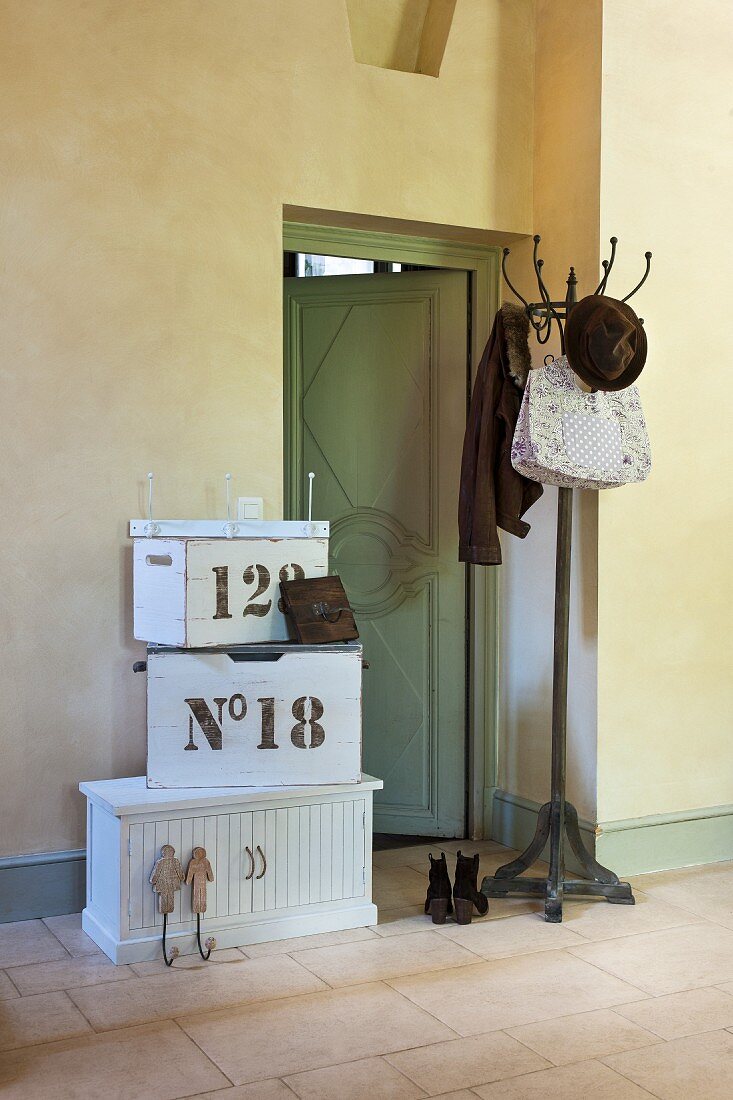 Bag, hat and jacket on coat stand next to open interior door and stacked white vintage wooden boxes