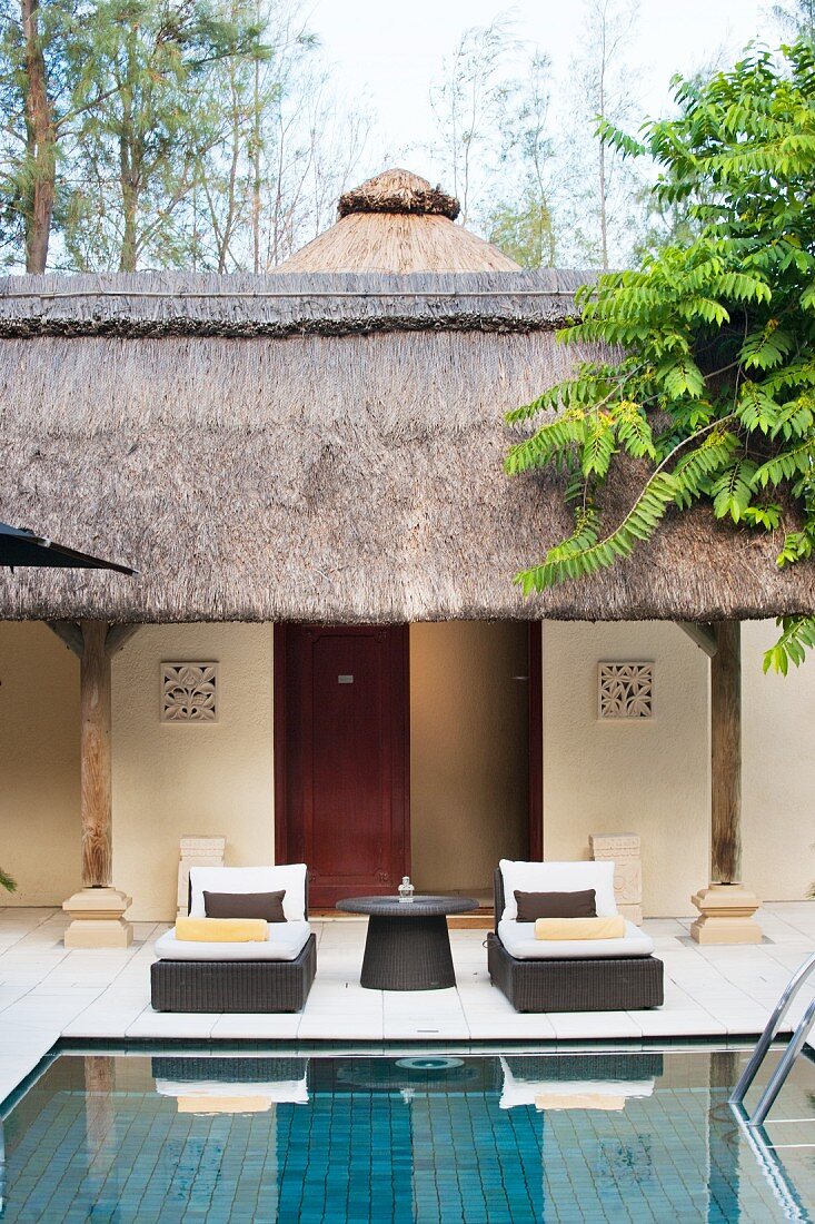 Loungers next to pool in courtyard with traditional thatched arcade