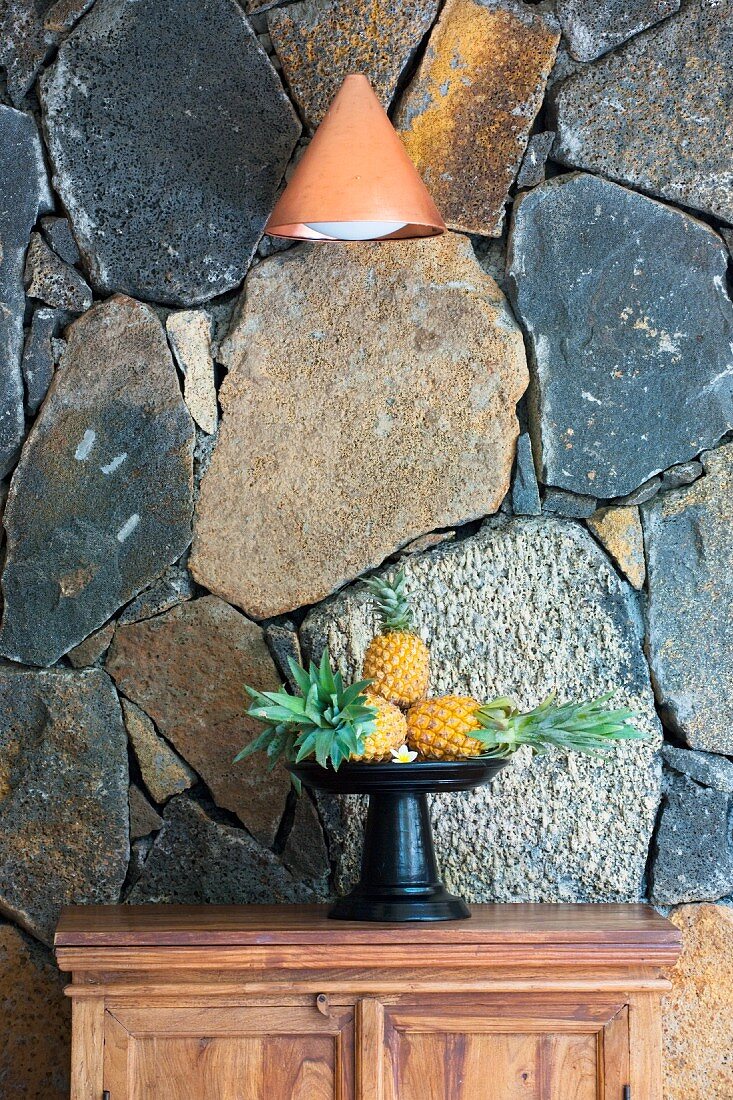 Schale mit Ananas vor einer rustikalen Natursteinwand